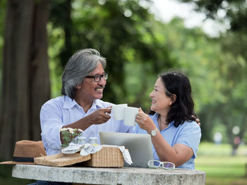 Happy couple toasting coffee cups on table at park