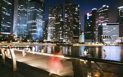 Illuminated city by river against sky at night