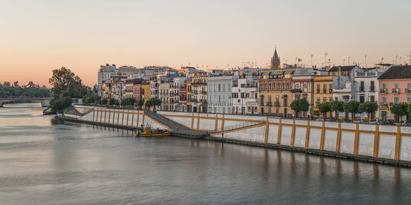 City by guadalquivir river against sky during sunset