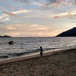 Boy playing on beach against sky during sunset