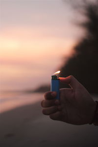 Close-up of hand holding sunglasses against sky during sunset