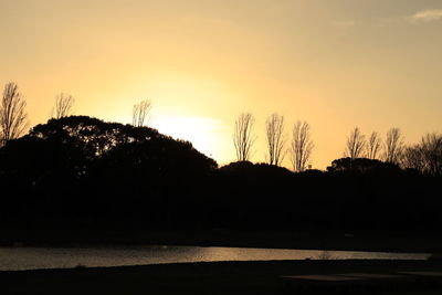 Silhouette trees by lake against sky during sunset