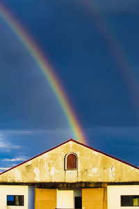 Low angle view of rainbow over building against sky