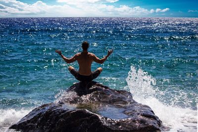 Rear view of man meditating at beach against sky