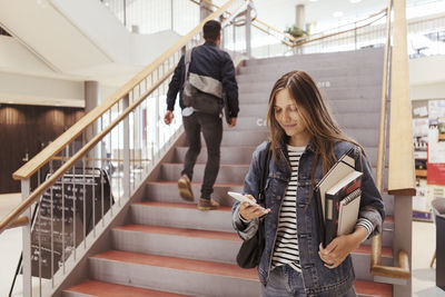 Female student using mobile phone while man walking up on steps in university