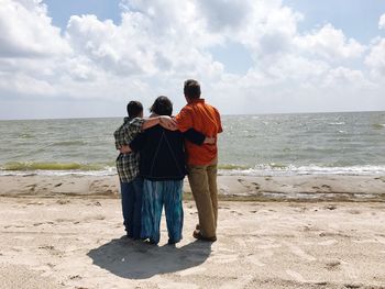 Rear view of family standing at shore against sky