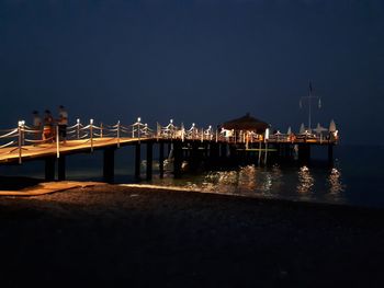 Illuminated pier over sea against clear sky at night