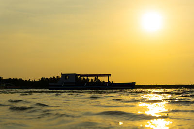 Silhouette ship in sea against orange sky