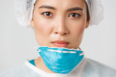 Close-up of young woman wearing mask against white background