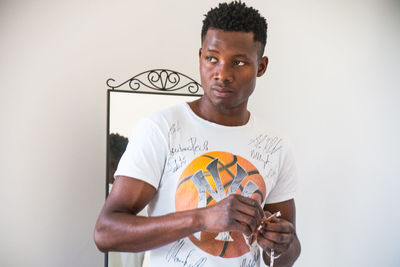 Portrait of young man holding eyeglasses against white background