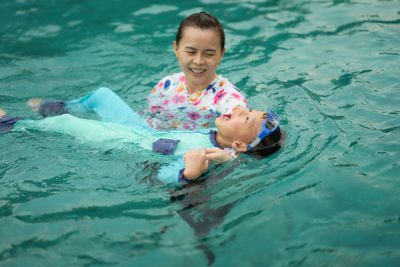 High angle view of mother looking at son floating on water in swimming pool