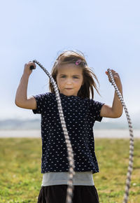 Portrait of girl holding rope standing on field against sky