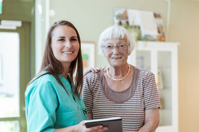 Portrait of smiling senior woman and nurse with digital tablet at home