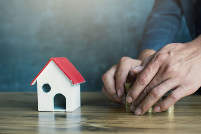 Cropped hands holding coins by model house at table