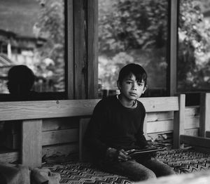 Portrait of boy using digital tablet while sitting on seat against window