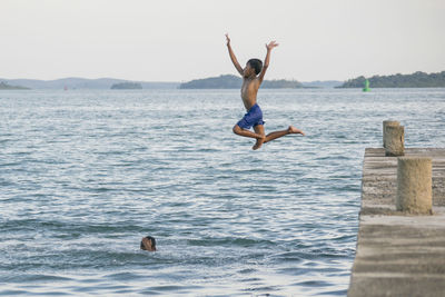 Full length of shirtless boy jumping in sea