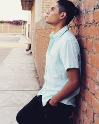 Side view of thoughtful young man leaning on brick wall