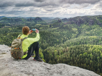 Man takes picture by phone. hiker walking in rocks with backpack and sunglasses. use trekking sticks