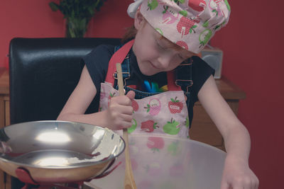 Girl wearing apron mixing flour in container on table at home