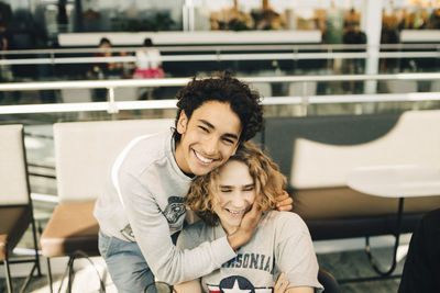 Portrait of cheerful teenage boy embracing friend in restaurant