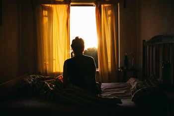 Rear view of woman sitting on bed at home