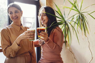 Portrait of smiling young woman holding drink while sitting at home