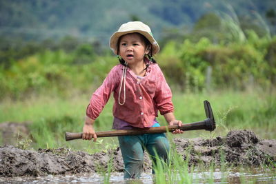 Girl holding shovel while standing at rice paddy