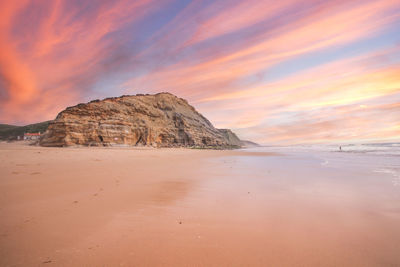 Rock formation on beach against sky during sunset