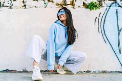 Portrait of smiling young woman sitting against wall