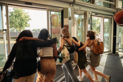 Rear view of teenage girls with arms around leaving shopping mall