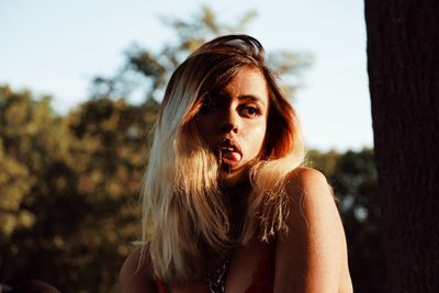 Beautiful woman sticking her tongue out against sky