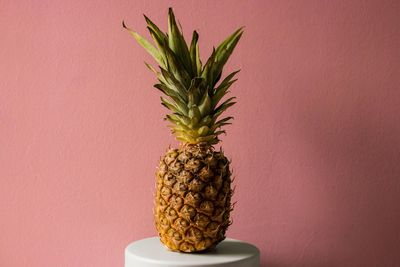 Pineapple on table against pink wall