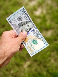 Cropped hand of man holding american paper currency over field