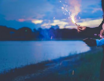 Woman holding sparkler by lake at night