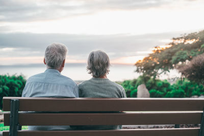 Rear view of woman sitting on bench against sky during sunset