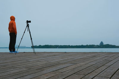 Man with tripod standing on pier over lake