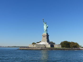 Statue of liberty by hudson river against clear blue sky