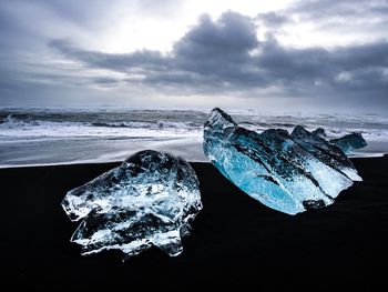 Close-up of ice on beach against sky
