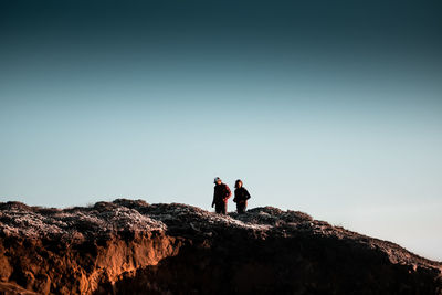 People standing on rock against clear sky