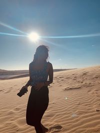 Woman standing on sand at sand dune against sky