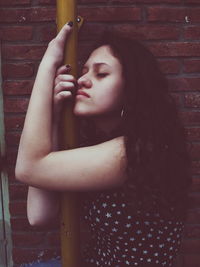 Young woman embracing pole against brick wall