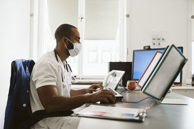 Male doctor using computer while sitting at desk during covid-19