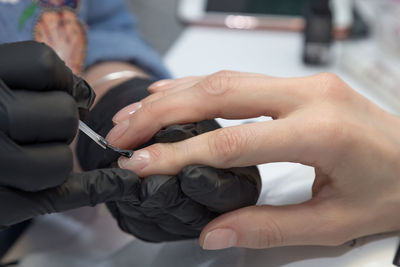 Cropped hands of manicurist applying nail polish on finger of woman