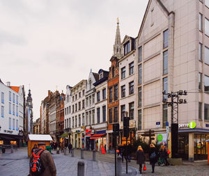 People walking on street amidst buildings in city against sky