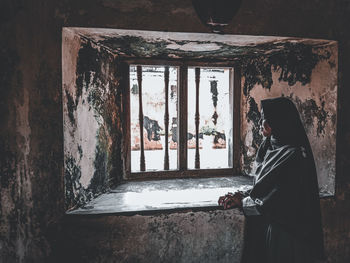 Rear view of girl standing against window in abandoned building