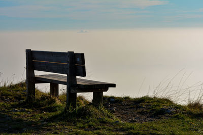 Empty bench on field against sky