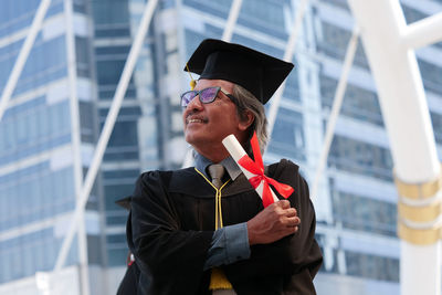 Businessman in graduation gown standing against office building