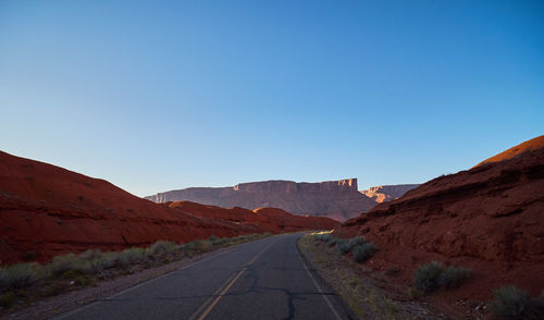 Road leading towards mountains against clear blue sky