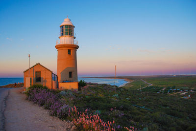 Lighthouse amidst sea and buildings against sky during sunset