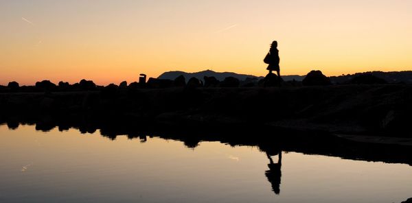 Silhouette woman standing by sea against sky during sunset